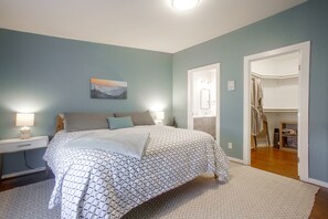 Quarto com cama, mesas de cabeceira, um quadro, banheiro com espelho e armário.
