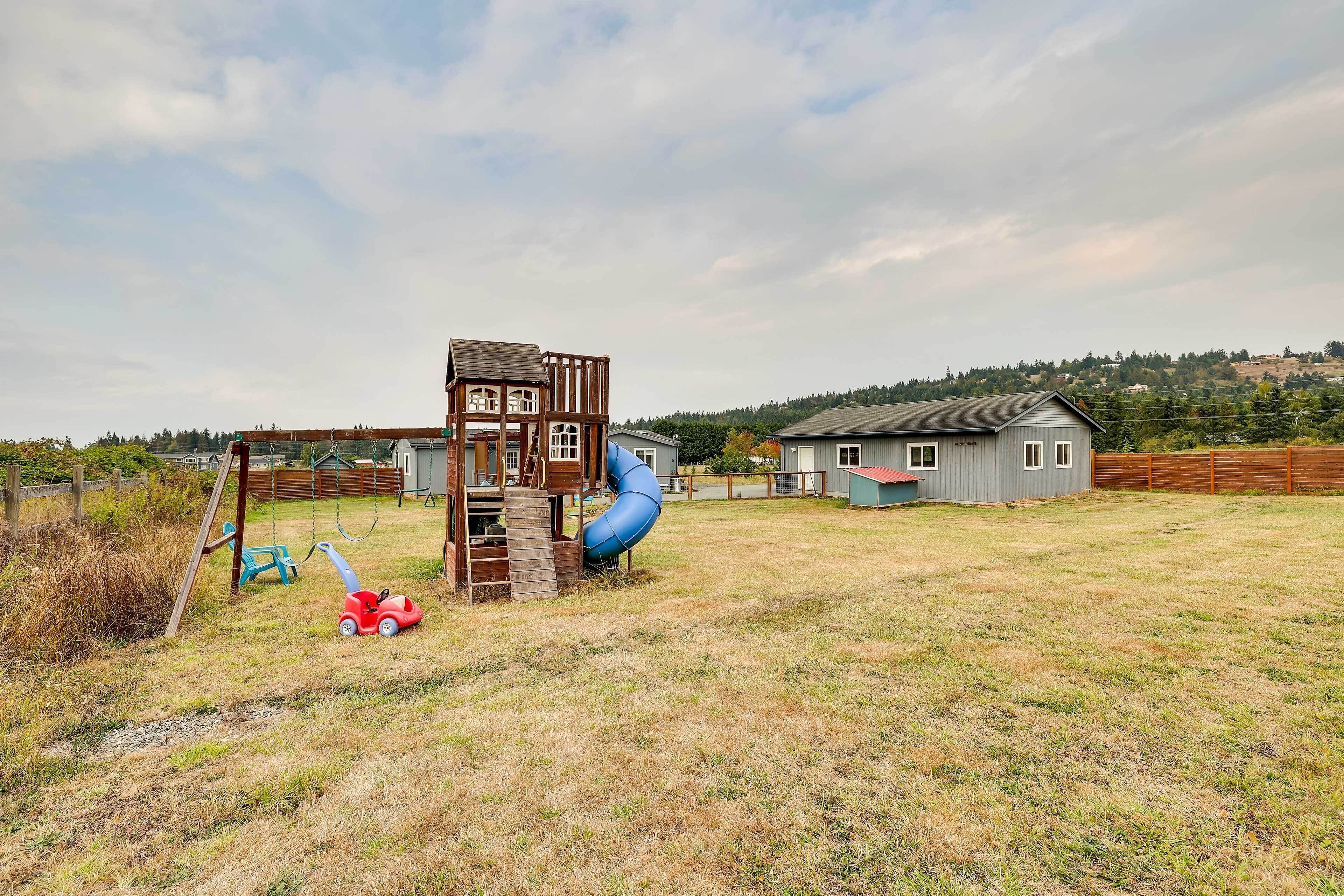 A playground with a slide and climbing structure, surrounded by a grassy yard and a house.