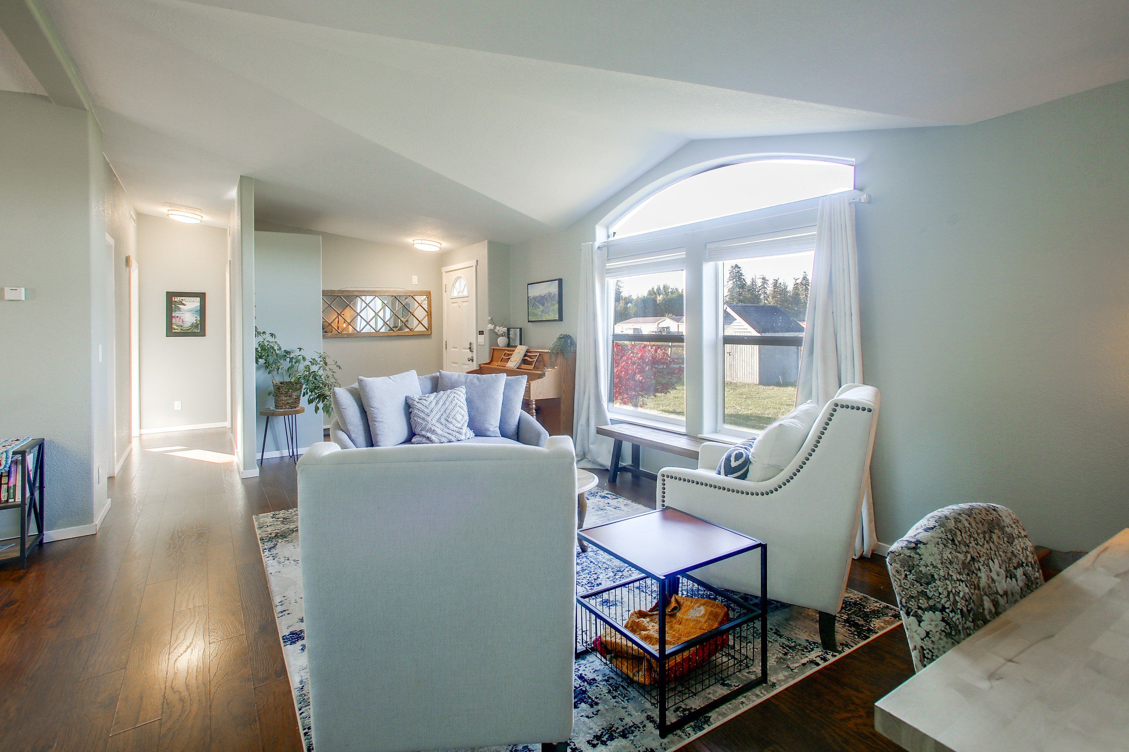 A spacious living room with a large window, a sofa set, a coffee table, and a pet bed.