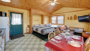 A cozy cabin with a checkered floor, wooden walls, a dining table set with plates and glasses, and a TV mounted on the wall.