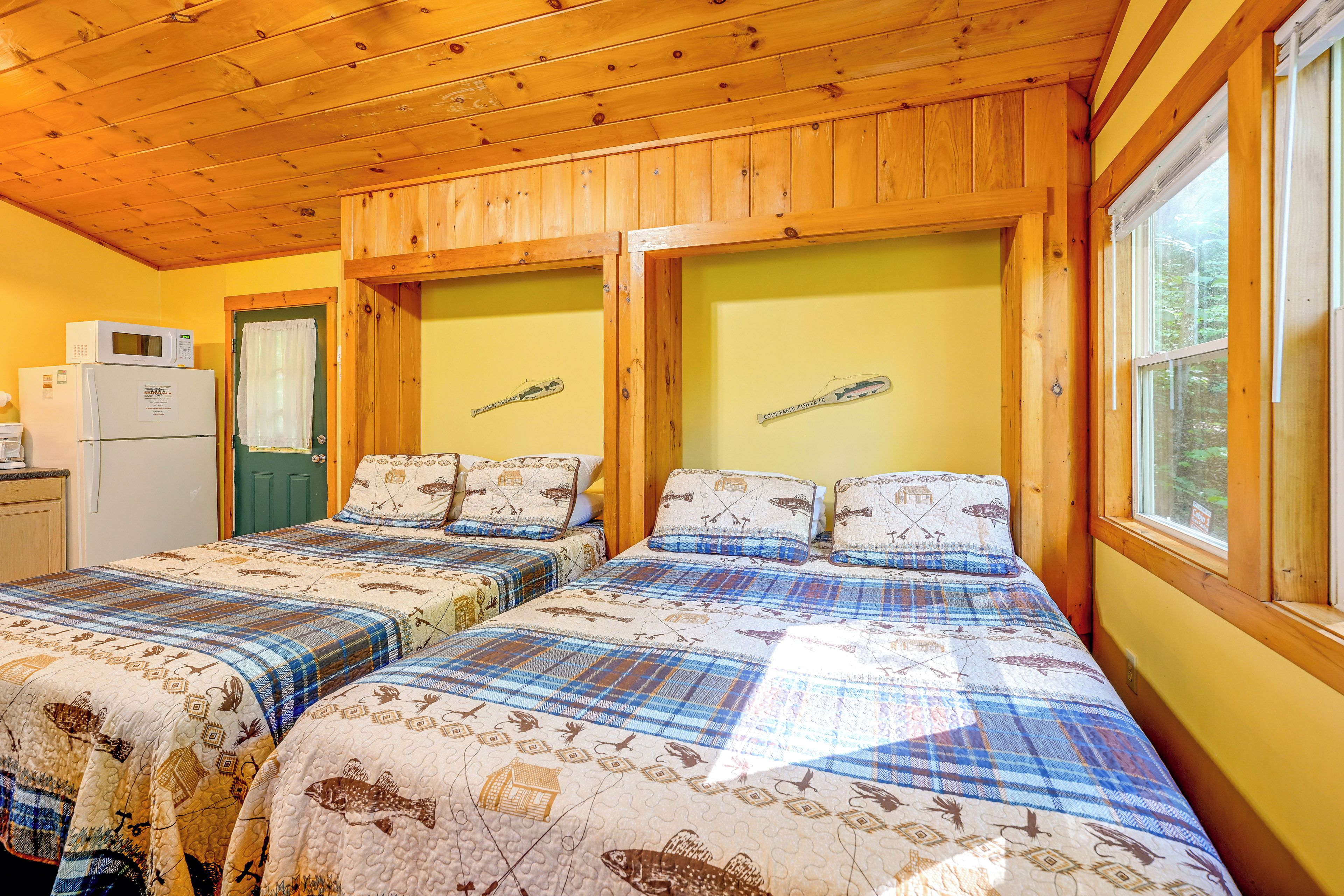 A cabin with two beds, a refrigerator, and a window with a view of trees.