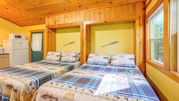 Eine Hütte mit zwei Betten, einem Kühlschrank und einem Fenster mit Blick auf Bäume.