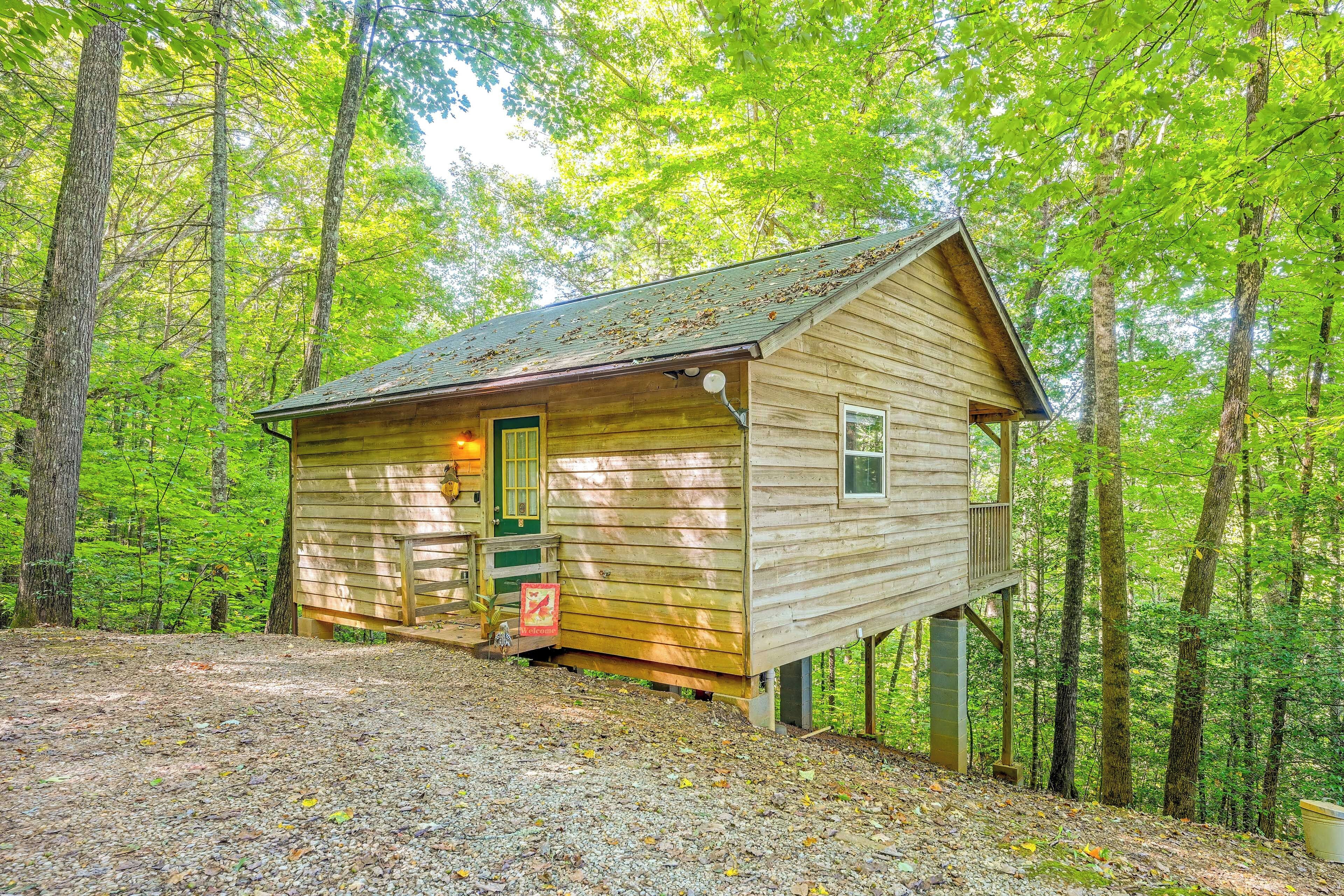 A wooden cabin with a green door, a small porch, and a welcome sign.