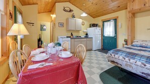 A cozy room with a dining table set for four, a bed with a patterned bedspread, a kitchenette with a microwave and refrigerator, and wooden ceiling beams.