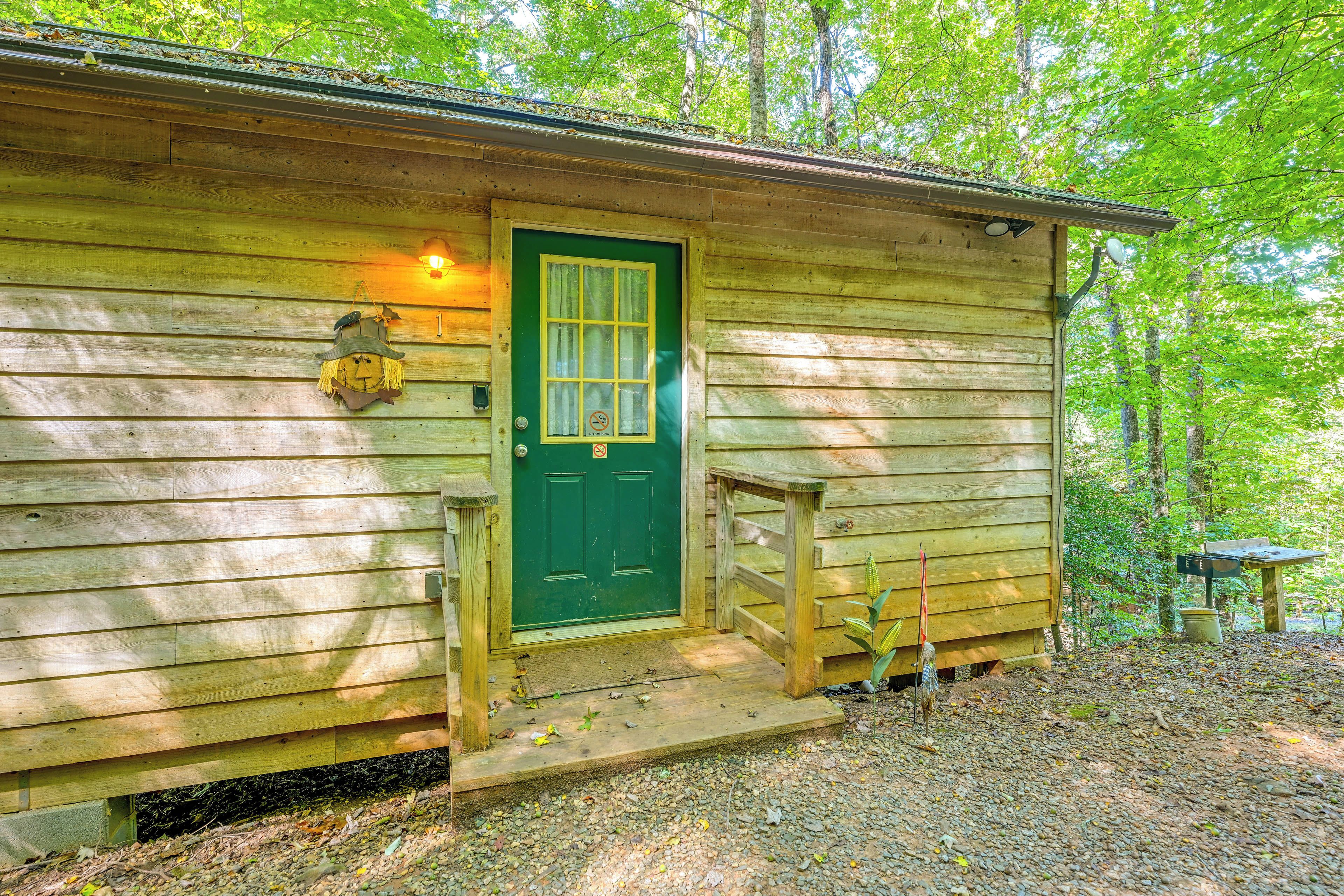 A wooden cabin with a green door, a small porch, and a window with a 'no smoking' sign.
