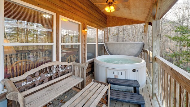 A wooden deck with a hot tub, wooden benches, and a ceiling fan.