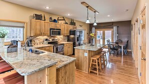 A spacious kitchen with wooden cabinets, a granite countertop, and a central island with stools. - Spacious Lead Getaway w/ Private Hot Tub & Deck! (Lead)
