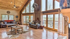 A spacious living room with a wooden ceiling, large windows, a mounted buffalo head, leather furniture, and a rustic rug. - Spacious Lead Getaway w/ Private Hot Tub & Deck! (Lead)