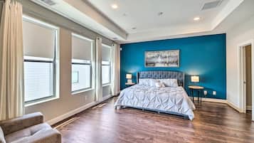 Un dormitorio con una cama grande, dos mesitas de noche, una ventana con cortinas y una pared de acento azul.