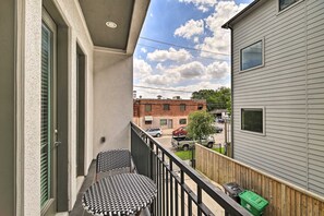 A balcony with a table and chairs, a view of a street with parked cars, and a building with a window. - 3 Mi to Daikin Park: Gated Houston Townhome (Houston)
