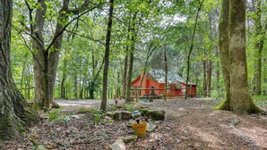 A forested area with a red building, surrounded by trees and a gravel path. - Serene Cabin w/ Riverfront Views & Access! (Fayetteville)