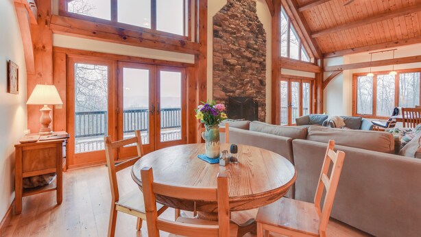 A cozy interior with a stone fireplace, wooden beams, and large windows. - Spacious Virginia Vacation Rental w/ Yard & Sauna (Purcellville)