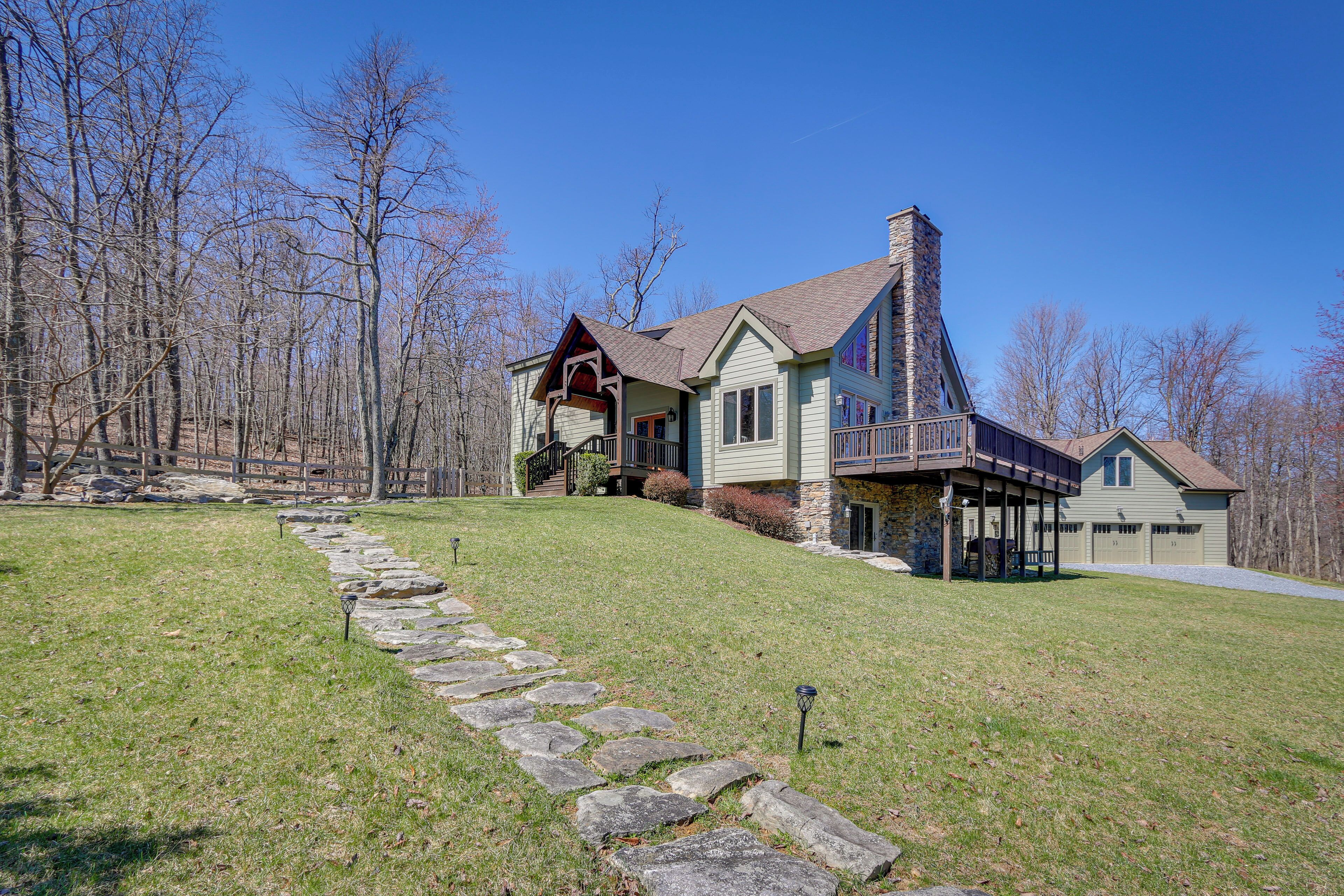 A large house with a stone staircase leading to the front door, surrounded by a stone wall and a grassy lawn.