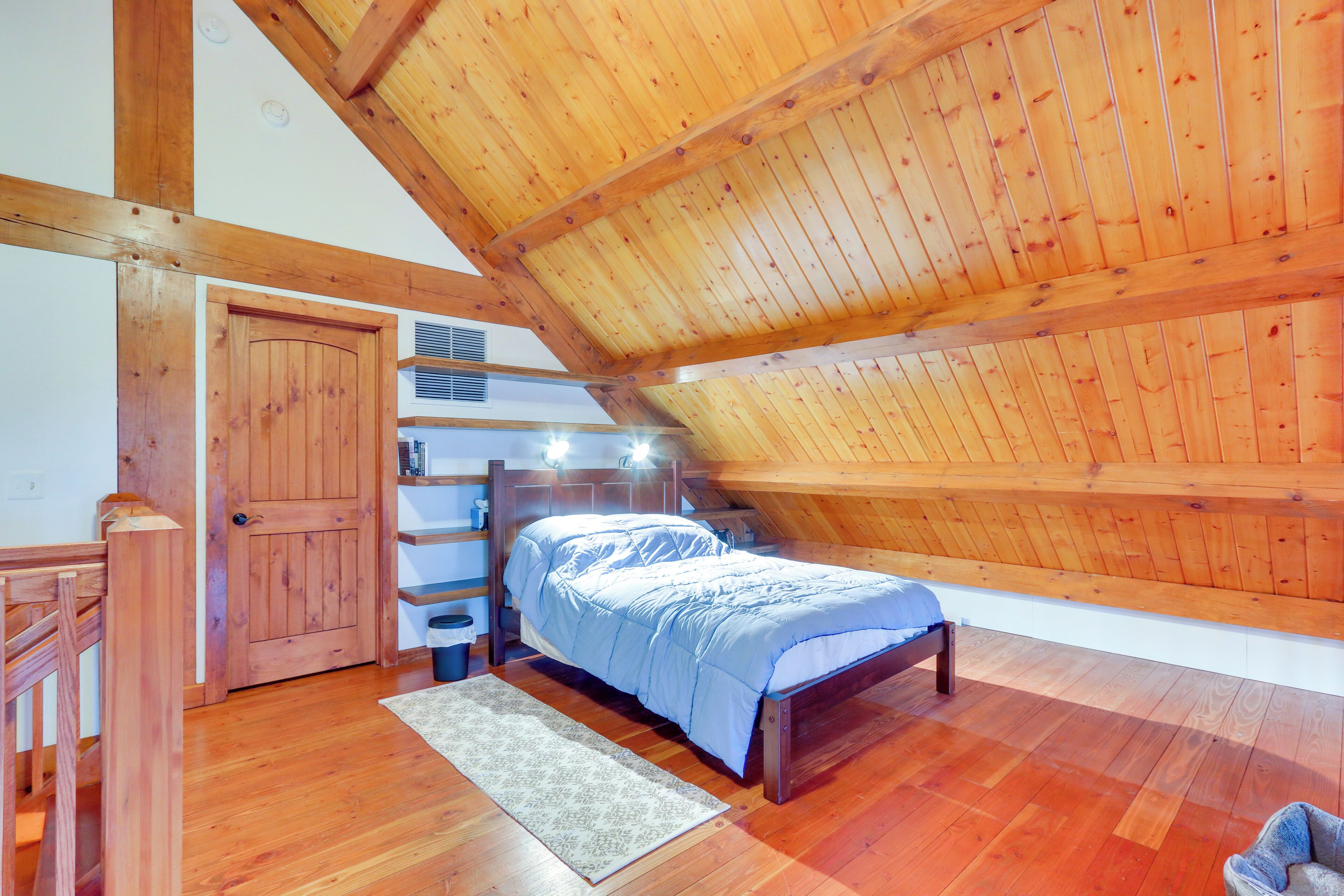 Une chambre avec un plafond en bois, un lit, une table de chevet et une étagère intégrée remplie de livres.