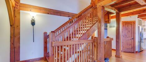 A wooden staircase with a railing, a light fixture on the wall, and a door leading to a kitchen area.
