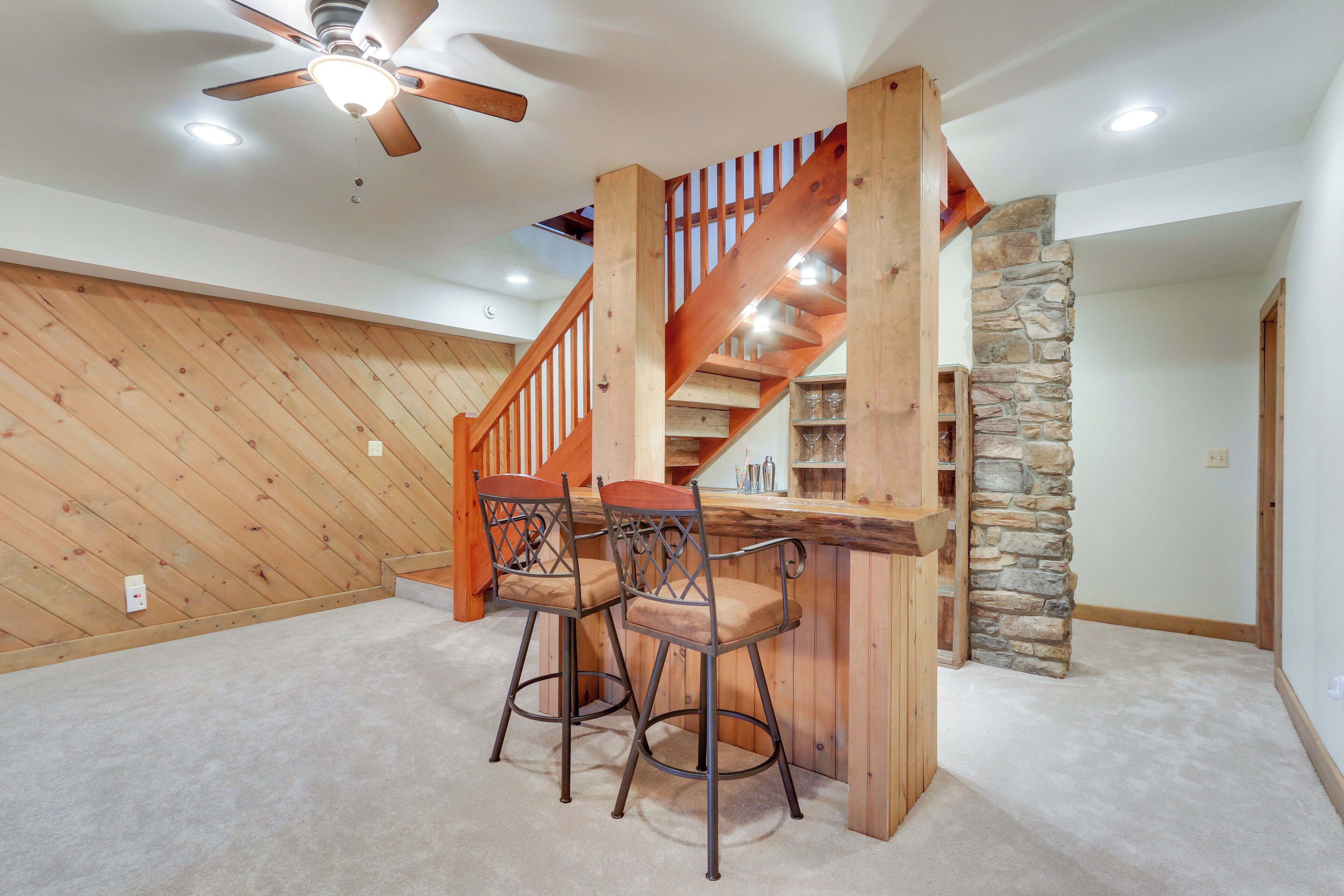 A wooden staircase with a stone wall, two bar stools, and a ceiling fan.
