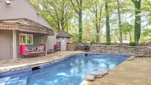 A swimming pool with a wooden deck, a covered seating area with a red chair, and a stone wall. - 15 Mi to University of Memphis: Getaway w/ Games (Southaven)