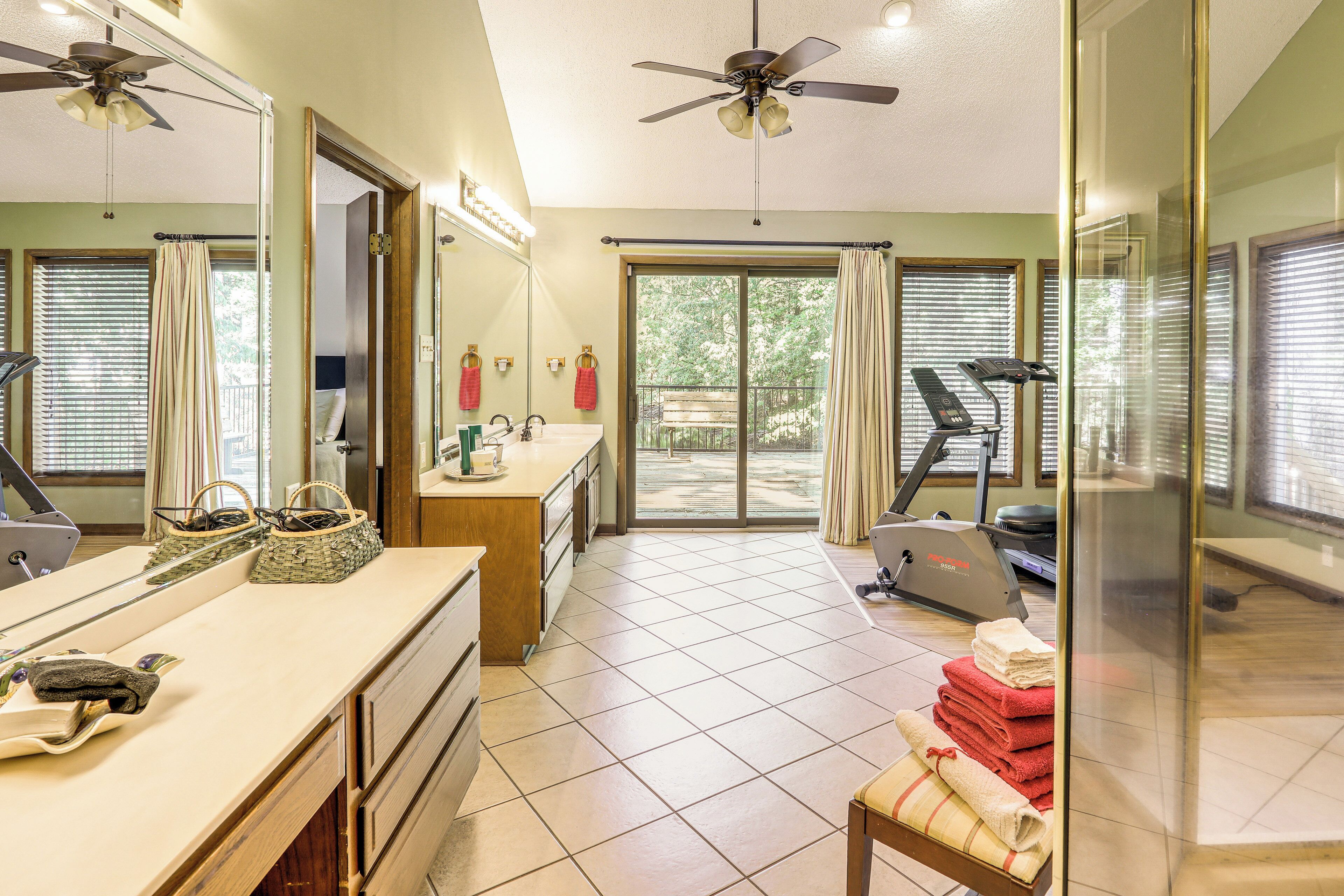 A bathroom with a vanity, a mirror, a ceiling fan, and a view of the outside.
