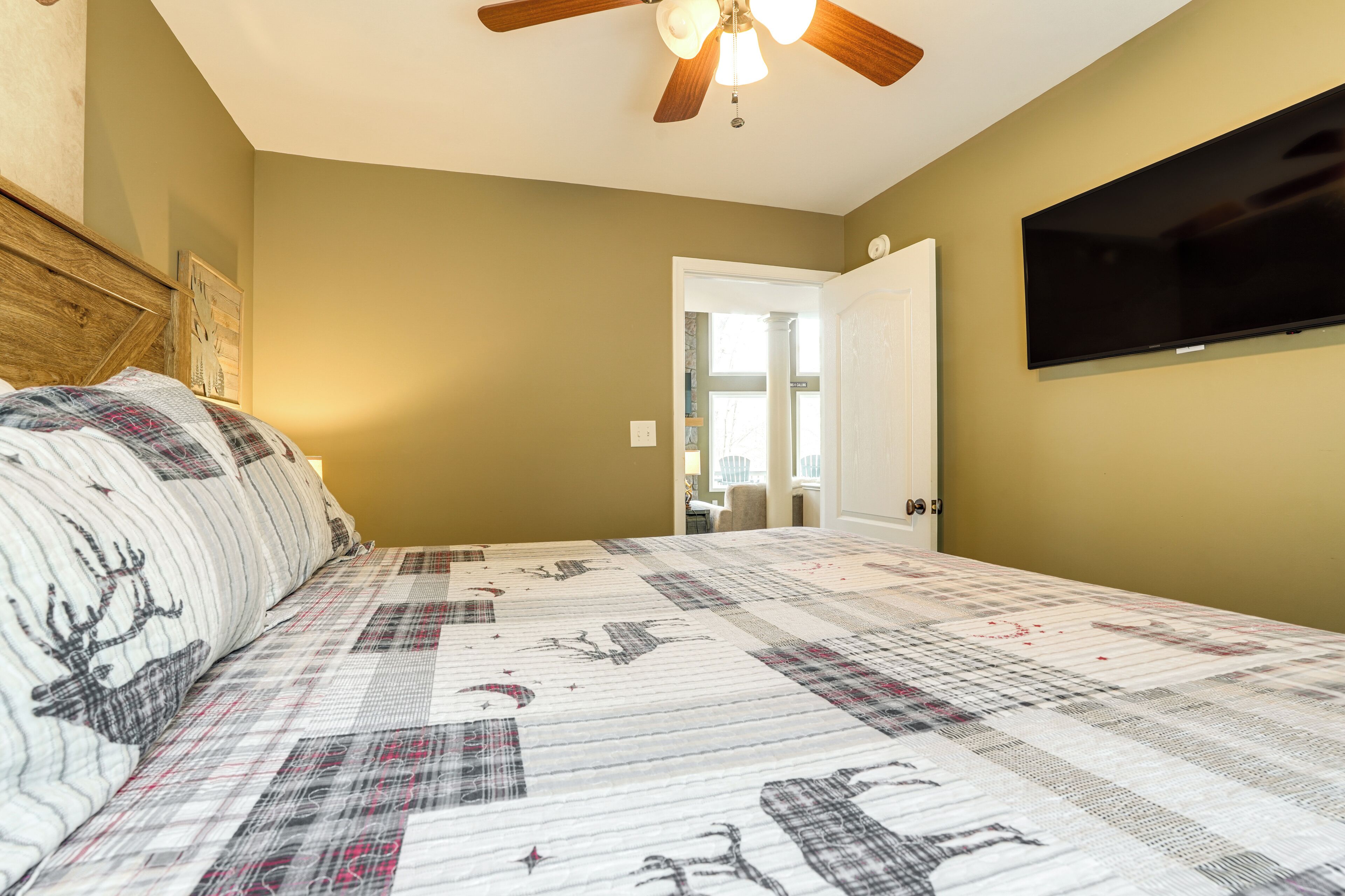 A bedroom with a bed, a ceiling fan, a television, and a door leading to another room.