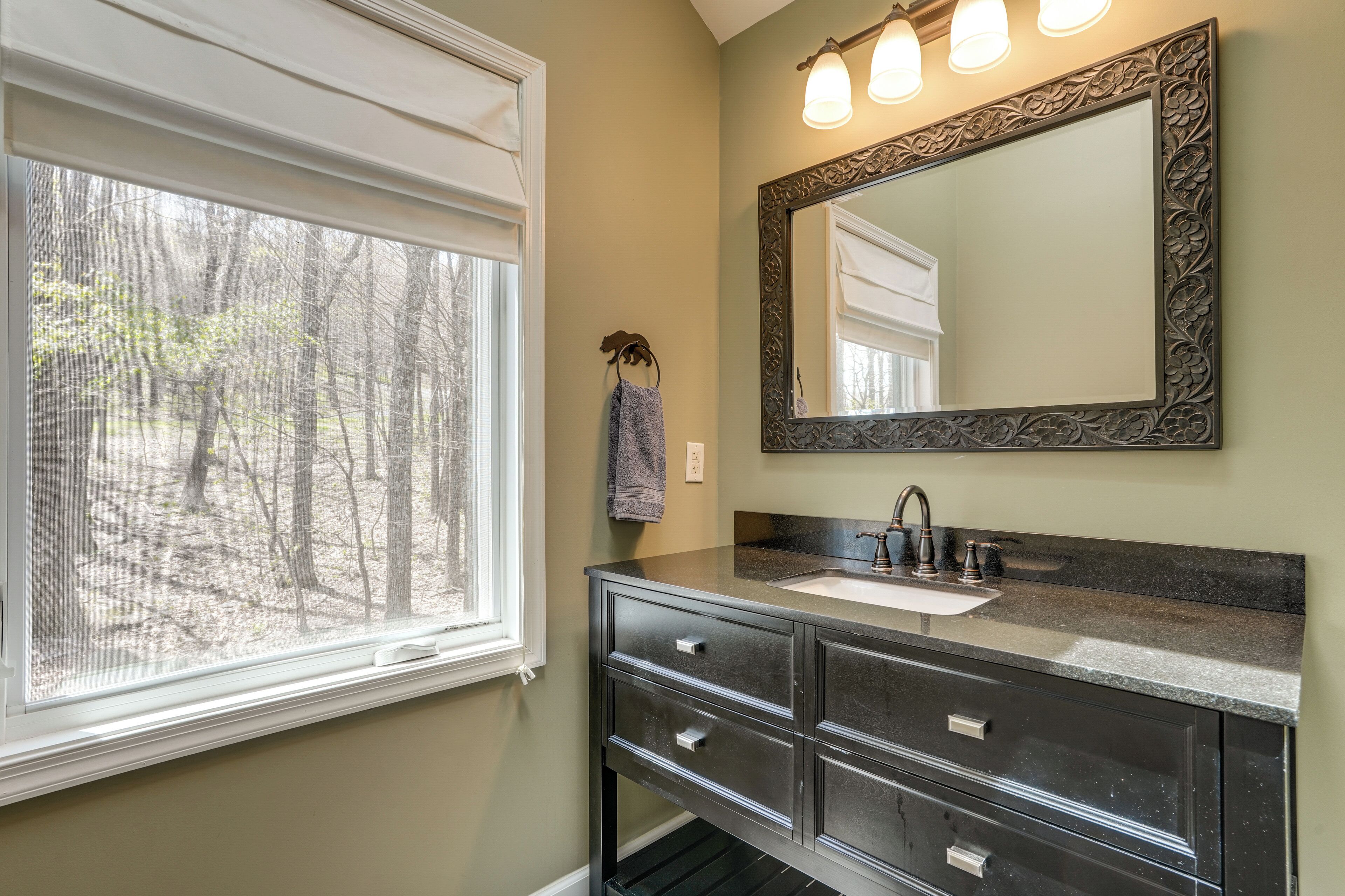 A bathroom with a large window, a sink, and a mirror with an ornate frame.