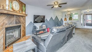 A living room with a fireplace, a sofa, a television, and a ceiling fan. - Hike, Golf & Explore: Ruidoso Retreat w/ Deck! (Ruidoso)