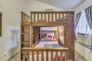 A bunk bed room with a built-in desk and a window with curtains.