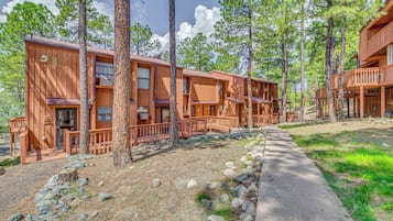 A row of wooden cabins with balconies, surrounded by trees and a gravel path.