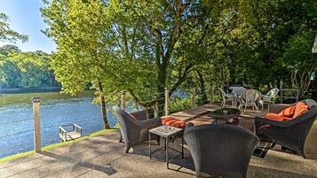 An outdoor patio with wicker furniture, a small table, and chairs overlooking a lake.