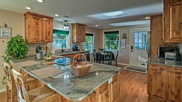 A kitchen with wooden cabinets, a marble countertop, and a dining area with chairs and a table.