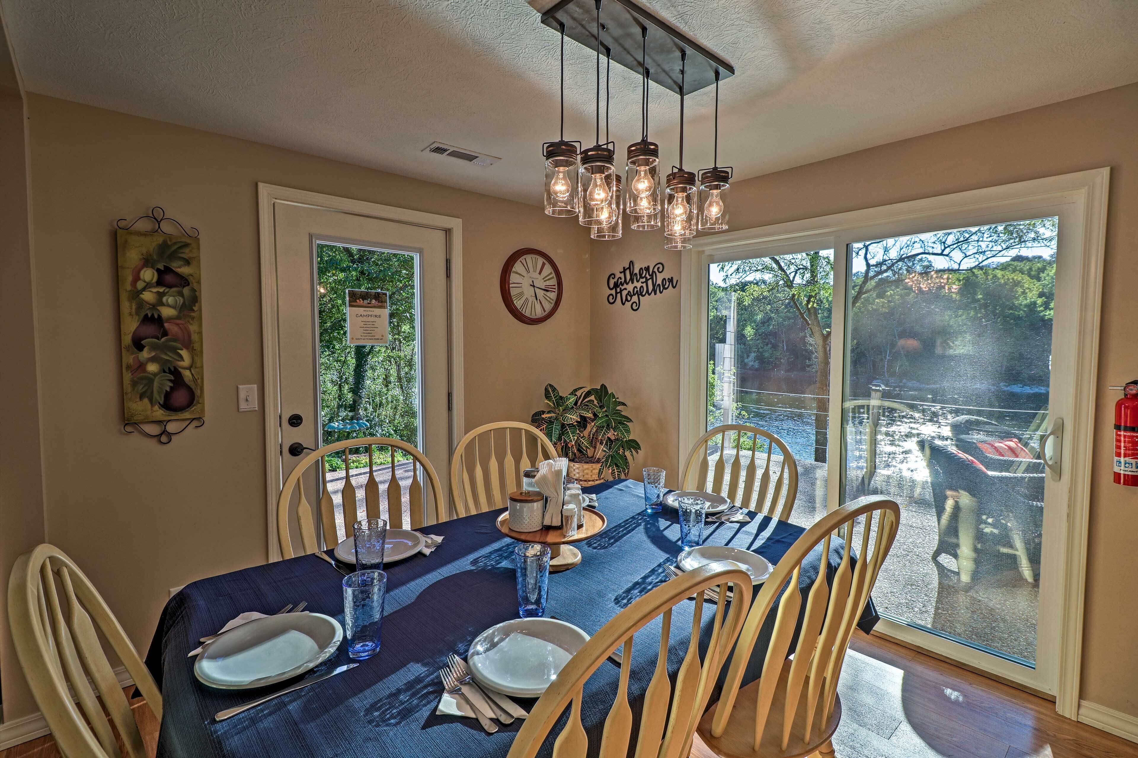 A dining area with a table set for six, chairs, a clock, and a sign on the wall.