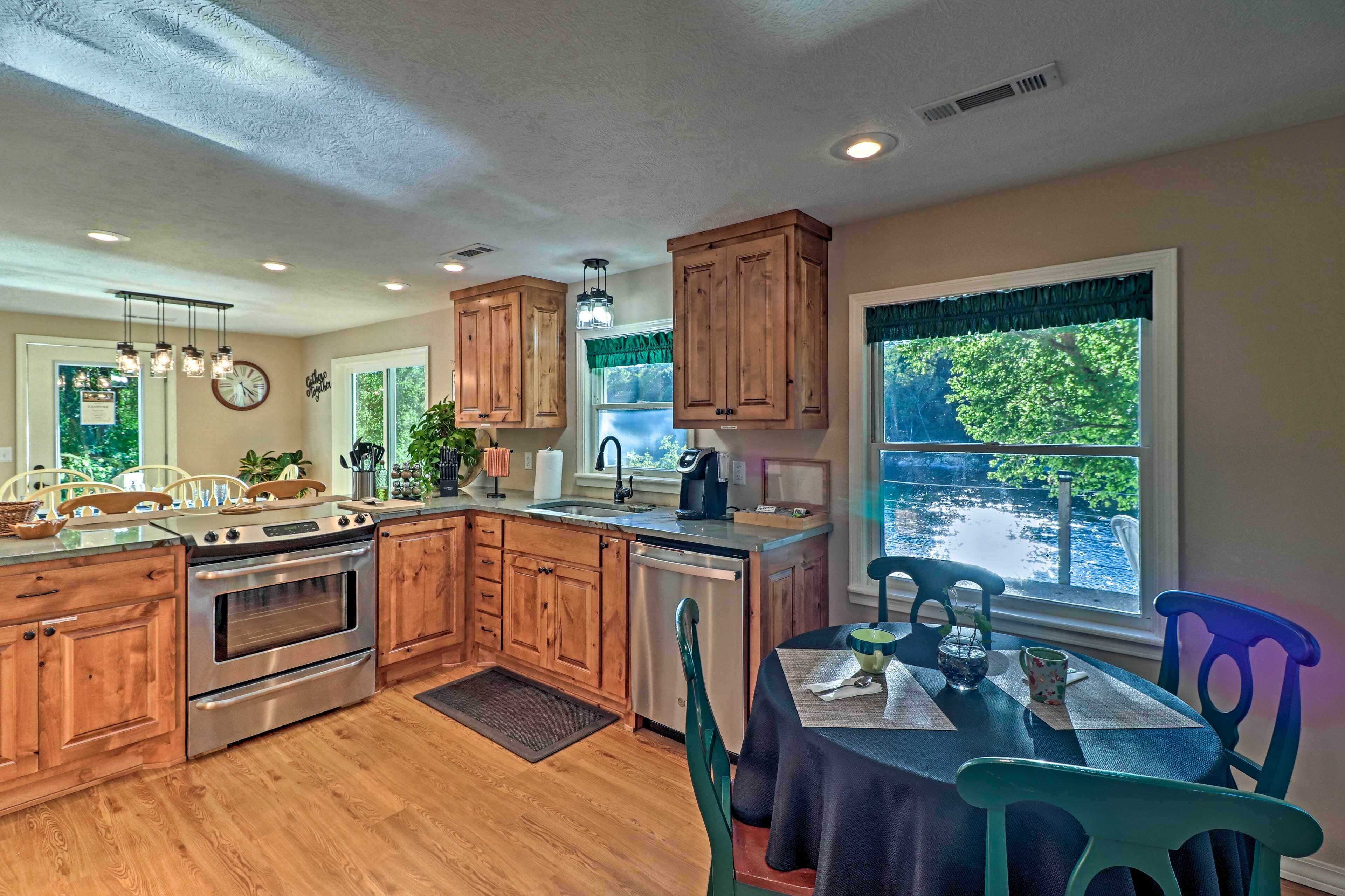 A kitchen with wooden cabinets, stainless steel appliances, a dining table with chairs, and a view of greenery outside.