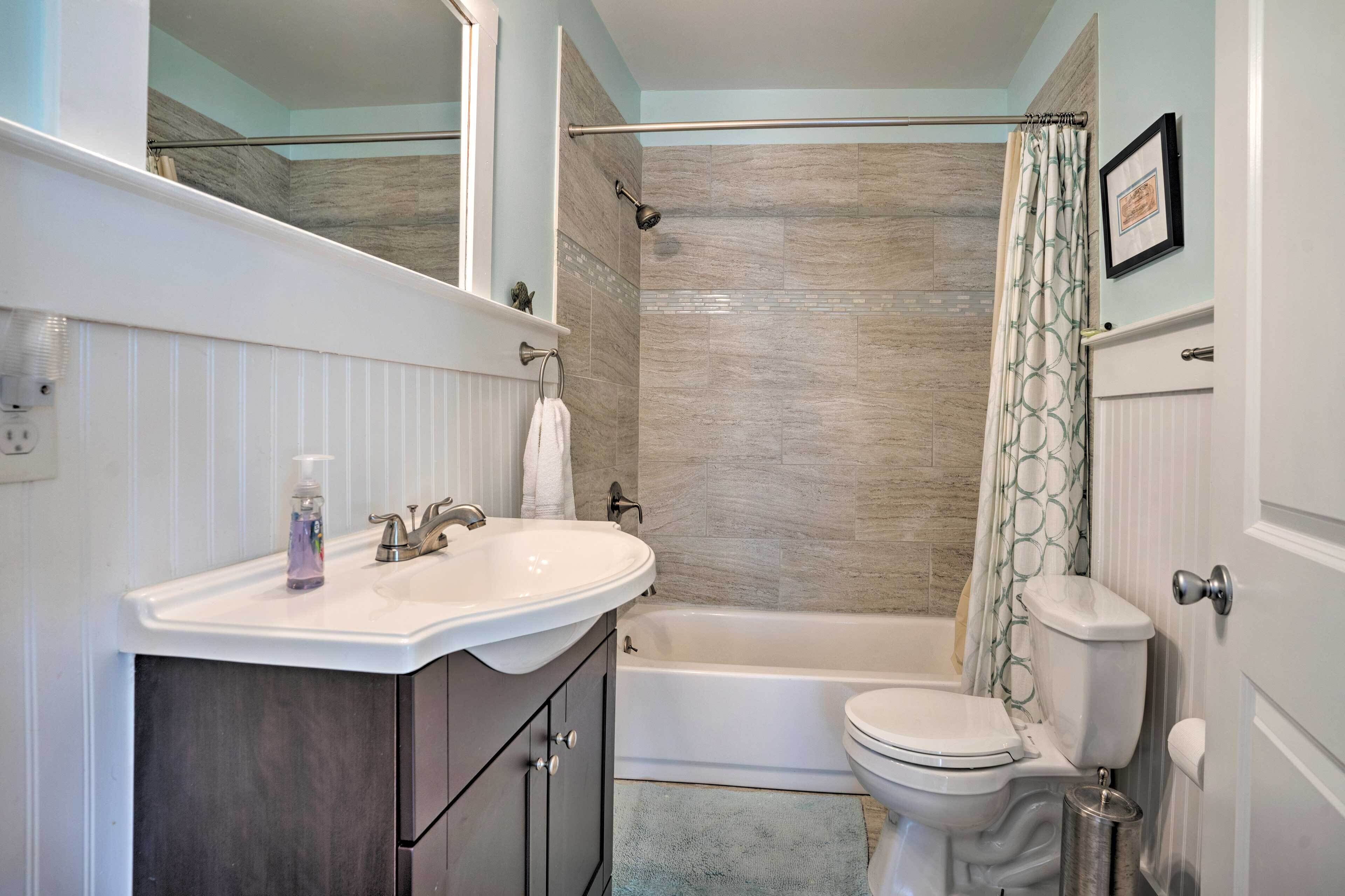 A bathroom with a white sink, vanity, bathtub, and toilet.