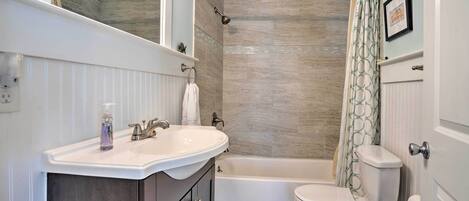A bathroom with a white sink, vanity, bathtub, and toilet.