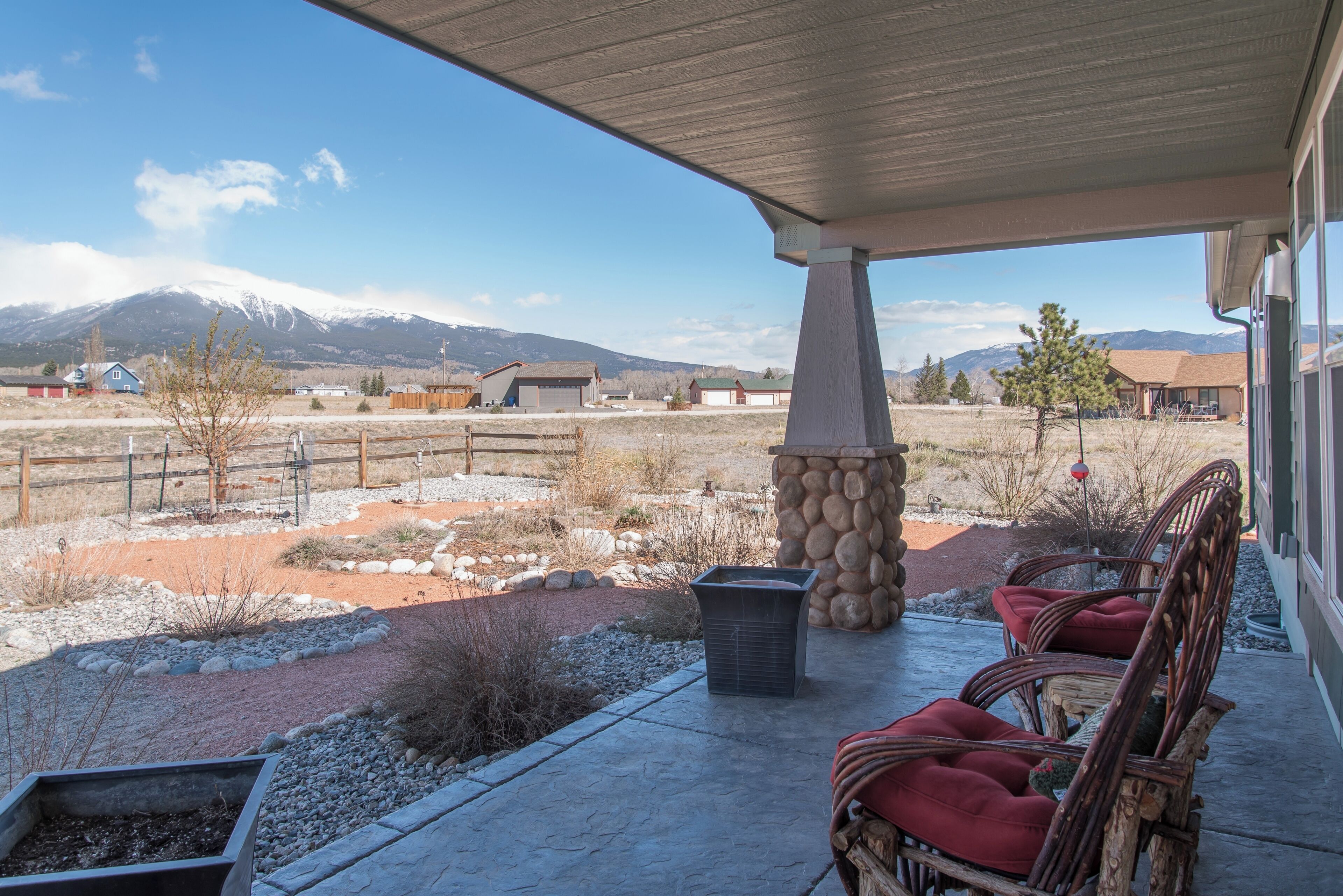 A covered patio with stone pillars, wicker chairs, and a fire pit.