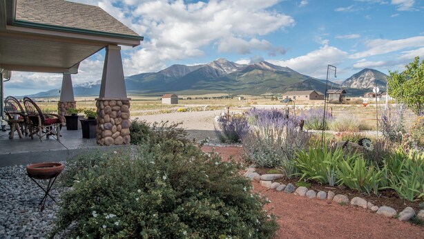 A covered patio with stone pillars, outdoor seating, and a garden with various plants and a gravel path. - 'the Fishing House' Buena Vista Home w/ Mtn Views! (Buena Vista)