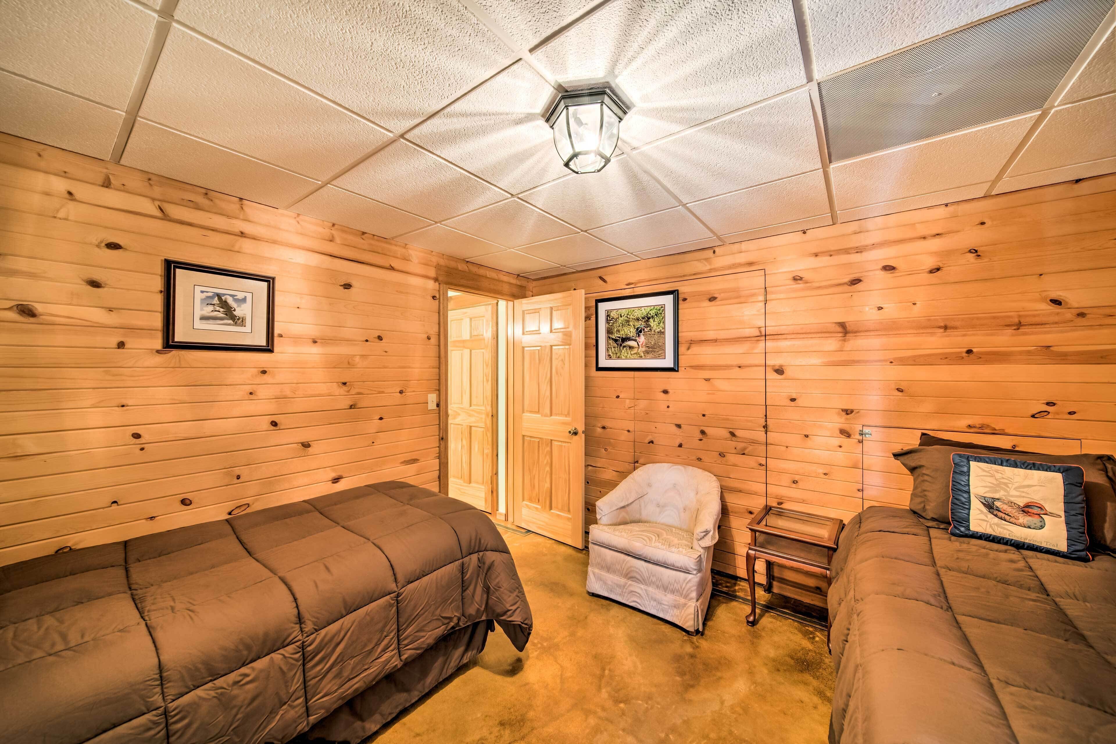 A room with wooden walls and a ceiling with recessed lighting. There are two beds with brown bedding and a small chair with a cushion.