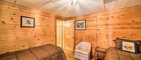 A room with wooden walls and a ceiling with recessed lighting. There are two beds with brown bedding and a small chair with a cushion.