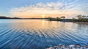 A calm lake at sunset with a dock and trees in the background. - Rustic Keosauqua Gem: Fire Pit & Lake Sugema Views (Keosauqua)