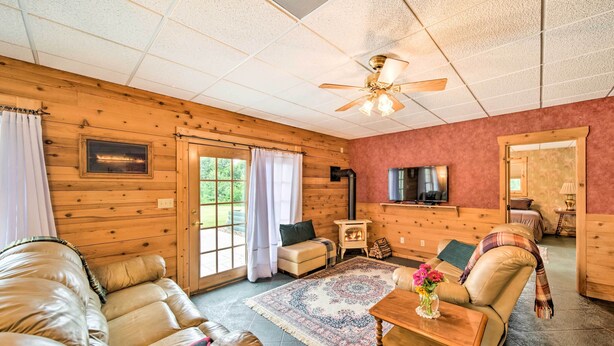 A cozy living room with a wooden floor, leather sofa, a patterned rug, and a television. - Rustic Keosauqua Gem: Fire Pit & Lake Sugema Views (Keosauqua)