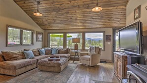 A spacious living room with a wooden ceiling, large windows, a sofa set, a TV, and a fireplace. - Updated Cabin w/ Hot Tub ~ 11 Mi to Winter Park! (Winter Park)
