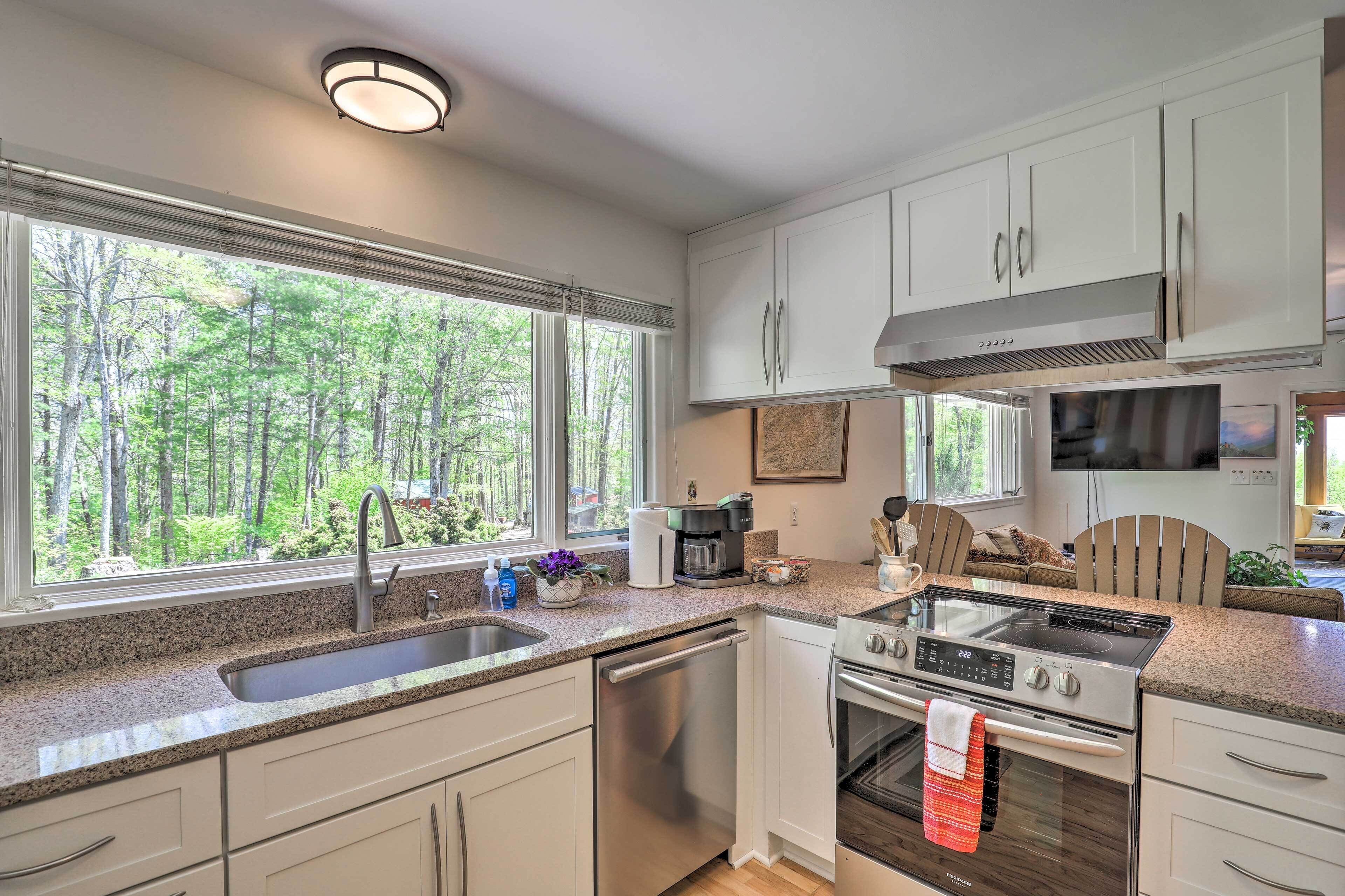 A modern kitchen with a large window, stainless steel appliances, and a view of a forest.