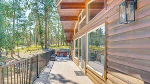 Une terrasse en bois avec une rambarde en métal, de grandes fenêtres et une vue sur une zone boisée.