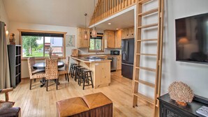 A modern kitchen with wooden cabinets, a central island, bar stools, a refrigerator, and a TV on a black stand. - Waterfront Cabin w/ 2 Boat Docks & Mtn Views! (St. Maries)