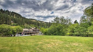 A large house with a spacious lawn in front, surrounded by trees and a forested hillside. - Waterfront Cabin w/ 2 Boat Docks & Mtn Views! (St. Maries)
