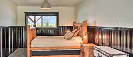 A bedroom with a wooden bed, a window, a hanging light fixture, and a vintage suitcase.