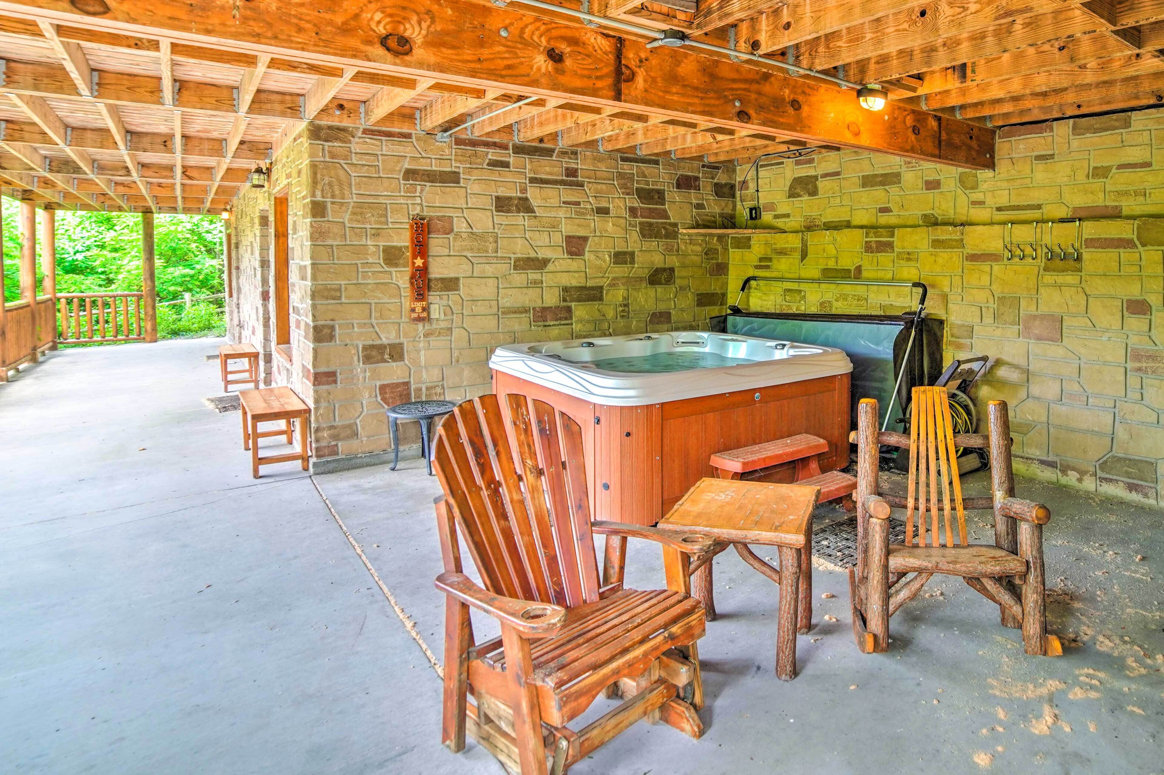 A rustic cabin with a stone wall, wooden ceiling, and a hot tub.