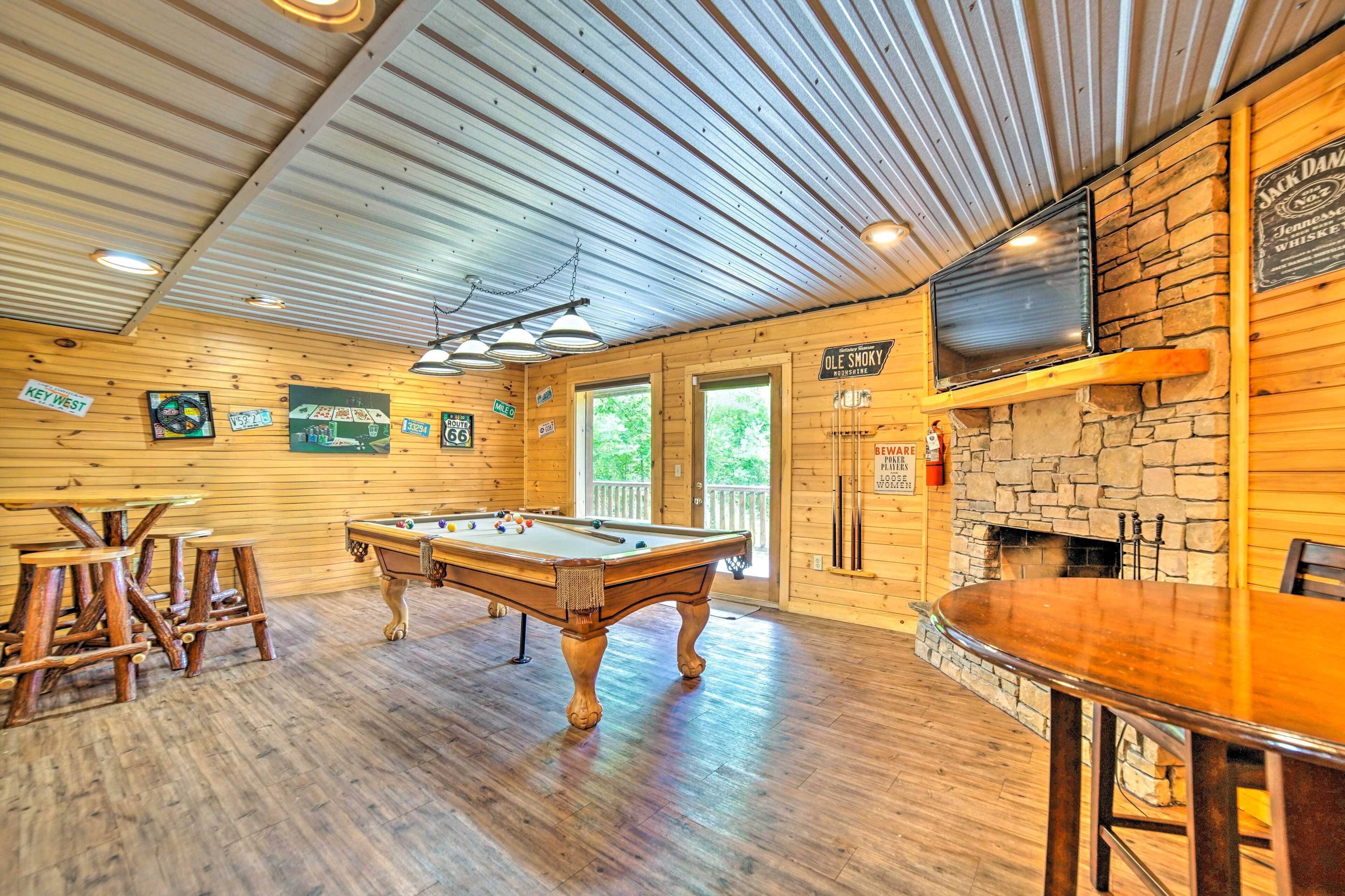 A wooden interior with a pool table, bar area, and a stone fireplace.
