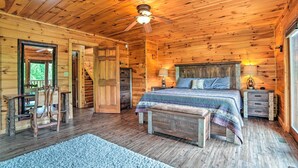 A wooden cabin bedroom with a bed, a chair, a nightstand, and a ceiling fan. - Games, Theater & Views: Gatlinburg Gem Near Trails (Gatlinburg)