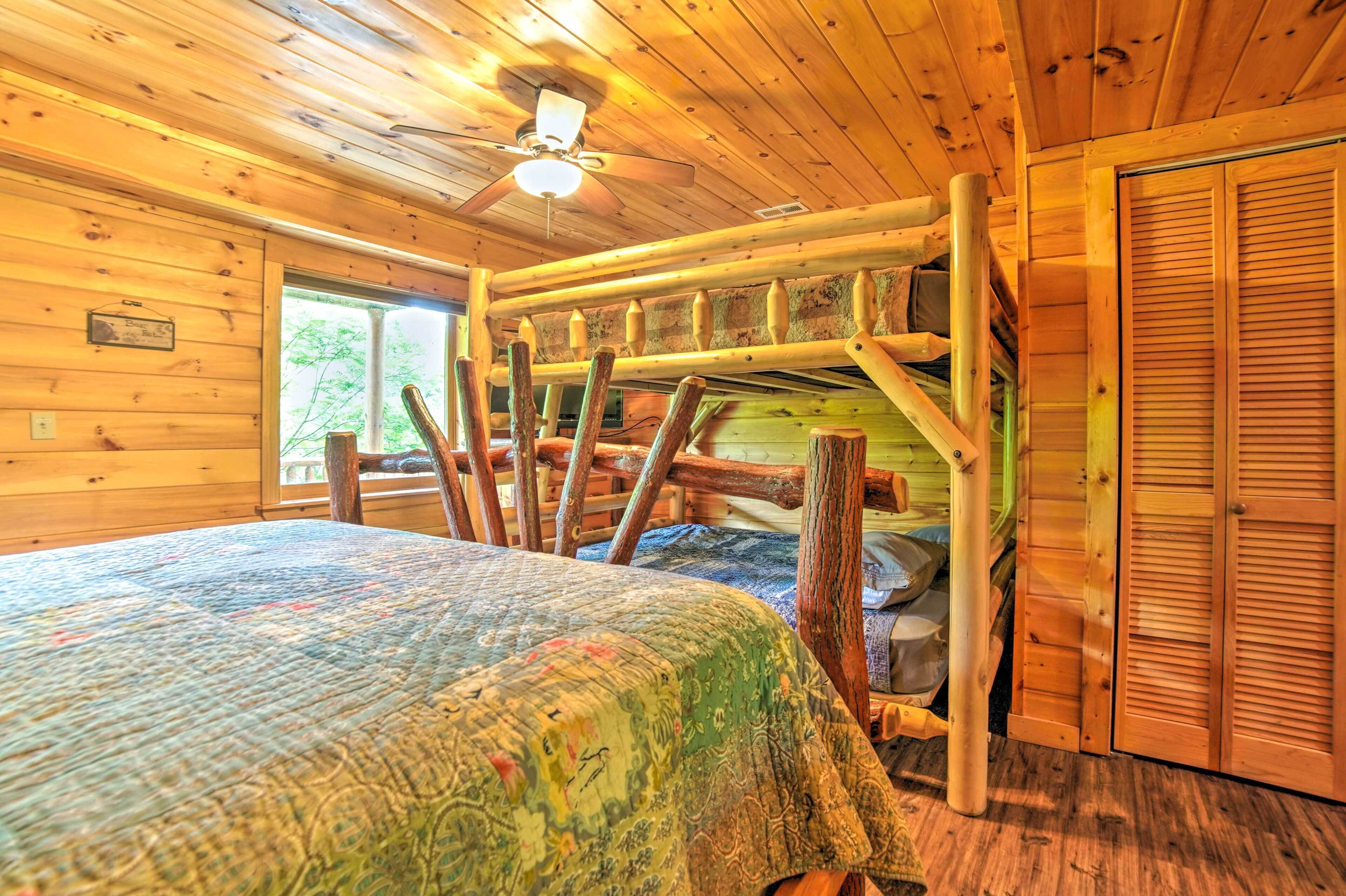 A log cabin bedroom with a bed, a ceiling fan, and a window.
