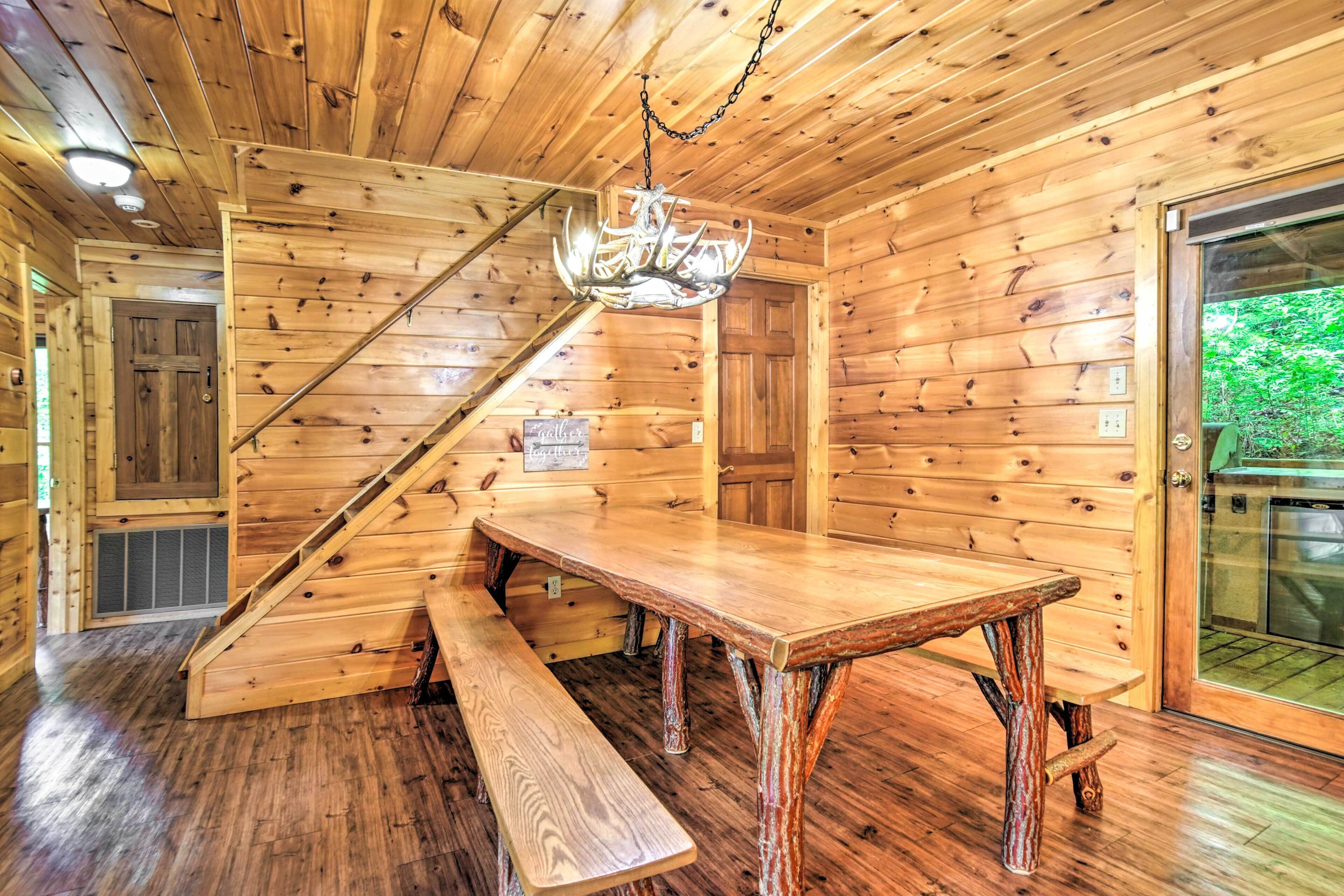 Een houten chalet van binnen, met een houten trap, een eettafel en bankjes.